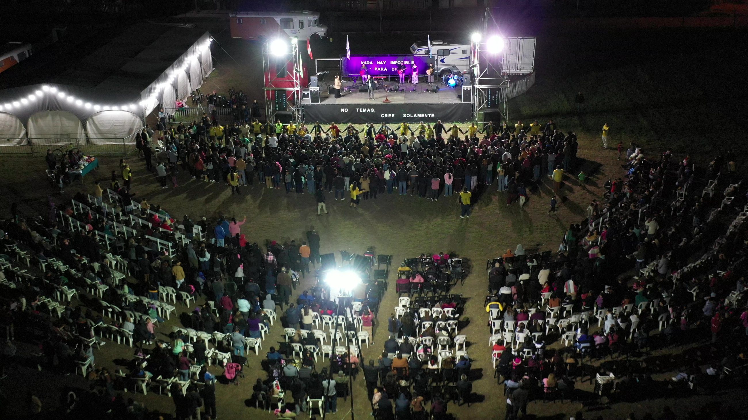 Vista aérea de campaña evangelística masiva nocturna con miles de personas reunidas